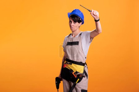 Photo for Serious woman builder with screwdriver and power drill posing in front of camera, holding building and renovating tools in studio. Female constructor acting confident with drilling tool. - Royalty Free Image