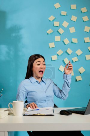 Photo for Female corporate employee laughing out loud while watching funny video on laptop sitting at work station. Woman relaxing in office at desk using internet after long busy day. - Royalty Free Image