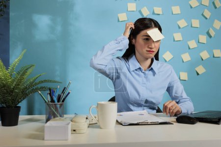 Photo for Dubious asian business woman scratching her head sitting at desk in office workspace. Uncertain company female worker sitting at work station with question mark on her forehead. - Royalty Free Image