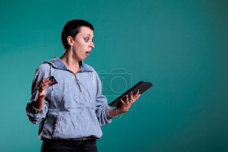 Foto de Mujer confusa haciendo compras en línea sosteniendo tableta escribiendo datos de la tarjeta de crédito que tienen dificultades después de ver los precios. Infeliz preocupado mujer pidiendo productos caros en el estudio - Imagen libre de derechos