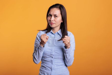 Photo for Aggressive filipino fighter doing self defense gesture in studio standing over yellow background. Defensive woman clenching fists ready to punch, expressing anrgy reaction preparing boxing - Royalty Free Image