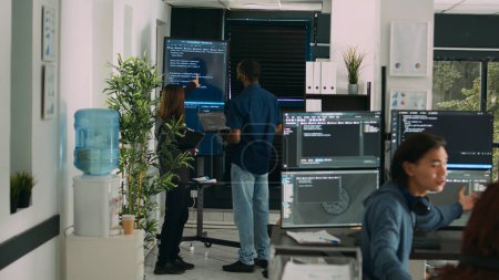 Photo for Diverse team of system developers analyzing code on big tv screen, checking errors in artificial intelligence project. Programmers working on machine learning software, developing new interface. - Royalty Free Image