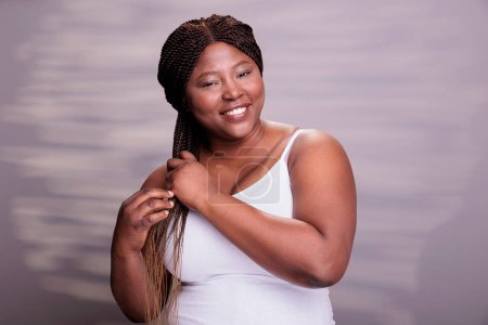 Photo for African american woman showing hair braiding technique, making african hairstyle tutorial. Natural beautiful plus size model smiling, looking at camera with carefree facial expression - Royalty Free Image