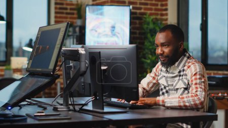 Téléchargez les photos : Artiste afro-américain de sexe masculin travaillant en studio pour créer une production CGI sur les logiciels et les compétences numériques. Designer d'agence créative utilisant une interface professionnelle pour développer des infographies. - en image libre de droit