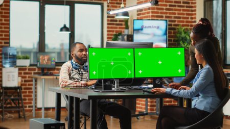 Téléchargez les photos : Une équipe diversifiée d'employées analysant des ordinateurs avec un modèle d'écran vert, des femmes regardant l'affichage de maquettes. Créateurs de contenu utilisant une clé chromatique isolée avec espace de copie vide sur les moniteurs. - en image libre de droit