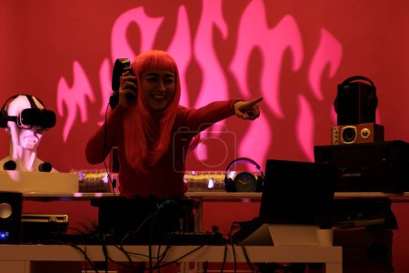 Téléchargez les photos : Artiste asiatique debout à la table dj exécutant chanson techno en utilisant des platines professionnelles appréciant jouer de la musique pendant la nuit dans le club. Interprète DJ faisant des performances avec l'équipement audio - en image libre de droit