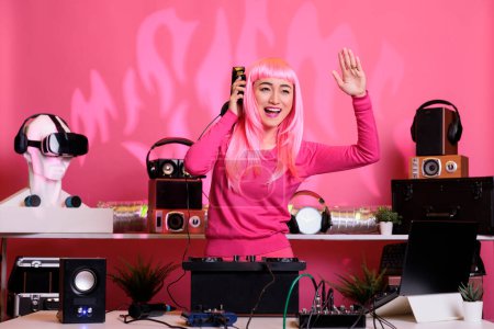 Téléchargez les photos : Femme aux cheveux roses dansant et s'amusant en club tout en jouant de la musique techno à la console de mixage professionnelle, profiter du mode de vie nocturne. Interprète DJ faisant des performances avec l'équipement audio - en image libre de droit