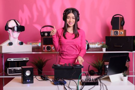 Photo for Positive performer standing at dj table doing approval gesture while mixing electronic music and techno using professional turntables. Artist playing stereo sounds with electronics and microphone - Royalty Free Image