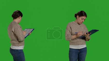 Photo for Close up of relaxed person checking clipboard files on camera, standing on green screen backdrop. Confident woman taking notes files writing information documents, working analysis. - Royalty Free Image