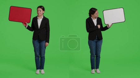 Téléchargez les photos : Femme d'affaires montrant bulle de parole pour créer une annonce en studio, portant costume de bureau formel et en utilisant carton. Gestionnaire tenant l'icône de carton de copyspace pour faire la publicité sur l'écran vert. - en image libre de droit