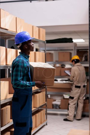 Photo for Mail sorting center worker holding packed cardboard box with client order. Shipping company african american man employee carrying carton and managing parcels transportation - Royalty Free Image