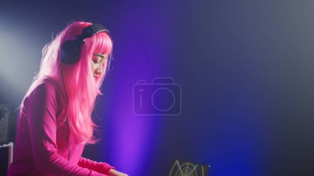 Foto de Dj in pink hair mixing electronic sound using mixer console, dancing and having fun in club with fans during performance. Asian artist performing techno music using professional audio equipment - Imagen libre de derechos