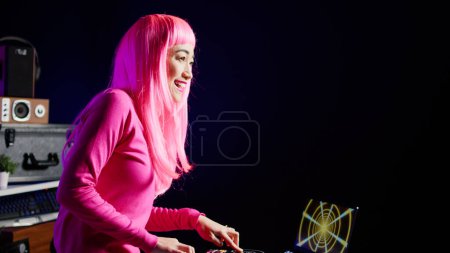 Téléchargez les photos : Musician with pink hair mixing and mastering techno sound using professional mixer console, performing music in nightclub. Performer playing electronic song, having fun during performance - en image libre de droit