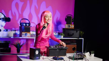 Photo for Performer having fun during performance talking with fans, mixing and mastering techno sound using professional mixer console. Dj musician with pink hair performing music in club at nightime - Royalty Free Image