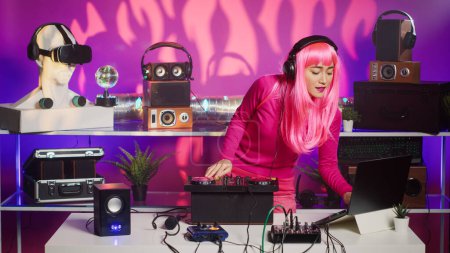 Téléchargez les photos : Musician with pink hair performing techno music using dj mixer console enjoying to play song with fans, having fun during night party. Artist doing performance with professional audio equipment - en image libre de droit