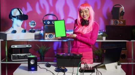 Photo for Artist holding vertically green screen chroma key tablet computer with isolated display, playing stereo sounds with electronics using professional turntables. Musician having fun in night club - Royalty Free Image