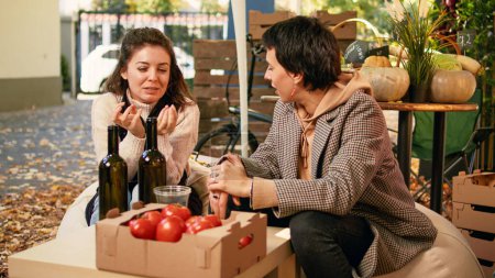 Verbraucherinnen sitzen mit einheimischen Bauern am Tisch und probieren hausgemachten Wein und genießen die Verkostung von Bioprodukten, bevor sie Produkte kaufen. Einkaufen auf Bio-Streetfood-Bauernmarkt.