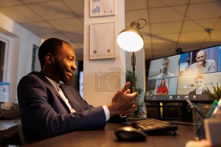 Photo for African american manager explaining investment graph to remote coworkers during online videocall meeting. Business team working late at night at marketing strategy in company statup office - Royalty Free Image
