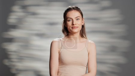 Téléchargez les photos : Cheerful woman embracing imperfections in studio, feeling sensual with natural radiant skin. Positive elegant person promoting self acceptance with skincare routine and products or cosmetics. - en image libre de droit