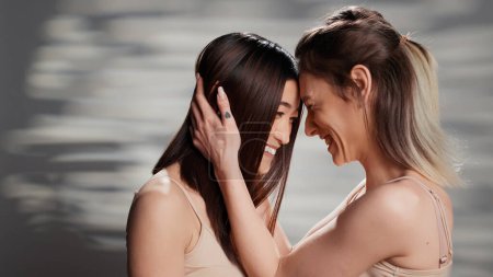 Photo for Beautiful natural women sharing hug in studio, feeling confident with bare skin and advertising self confidence. Interracial girls promoting beauty products and routine on camera, self love. - Royalty Free Image