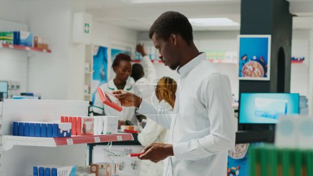 Téléchargez les photos : Male client looking at health vitamins in pharmacy, checking packs of medicaments and supplements. Young person buying pharmaceutical pills from drugstore shop, healthcare retail store. - en image libre de droit