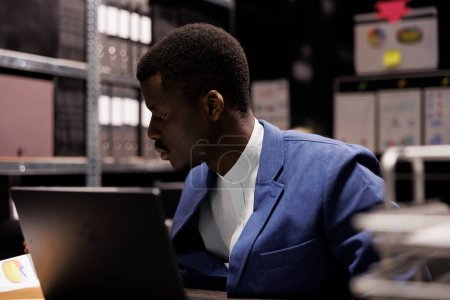 Photo for African american inspector trying to solve police case, analyzing crime scene evidence in arhive room. Private detective working late at night in criminology department. Investigation concept - Royalty Free Image