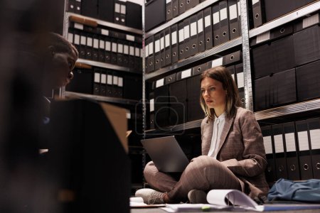 Photo for Depository workers discovering bookkeeping record in storage room, discussing administrative report. Diverse businesspeople analyzing management files, checking accountancy documents - Royalty Free Image