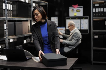 Foto de Contable asiático profesional revisando los datos analíticos burocráticos papeleo en la oficina del gabinete de archivos rodeado de informes estadísticos de contabilidad. Empresaria en repositorio de almacenamiento - Imagen libre de derechos