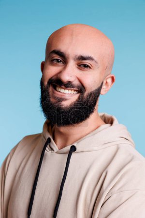 Photo for Smiling young arab man with cheerful facial expression portrait. Bald bearded arabian person with carefree joyful emotions wearing casual beige hoodie and looking at camera - Royalty Free Image