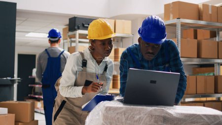Photo for Warehouse employees planning shipment on laptop, working in storage room depot with merchandise in boxes. African american people checking stock logistics for business distribution. - Royalty Free Image