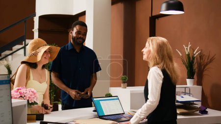 Photo for Hotel concierge greeting tourists at reception upon their arrival, welcoming guests at luxury tropical resort. Receptionist preparing to check in guests, providing excellent service. - Royalty Free Image