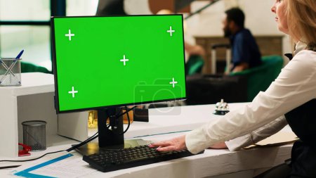 Photo for Receptionist using greenscreen pc at front desk lobby, looking at isolated display with chroma key template. Hotel concierge at reception checking mockup copyspace on computer. - Royalty Free Image
