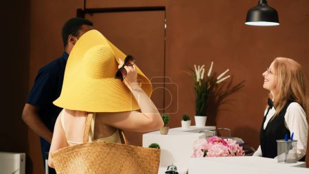Photo for Hotel worker registering couple at front desk, finding booking information and doing check in process. Female concierge at tropical resort reception working on guests accommodation. - Royalty Free Image
