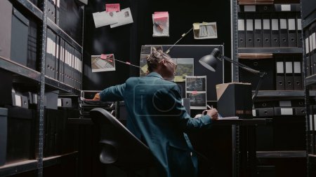 Photo for Private inspector reviewing clues on wall map to solve crime or felony, doing detective work in incident room. Law officer looking at criminal records, trying to uncover important details. - Royalty Free Image