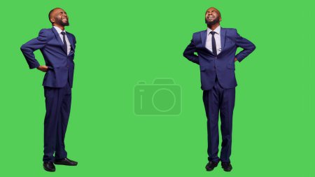 Photo for Male office worker suffering from spine pain in studio, dealing with backache and tension over full body greenscreen. Startup manager having backpain, unwell man in discomfort. - Royalty Free Image