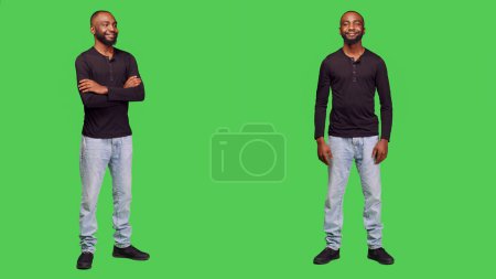 Photo for Optimistic adult standing over green screen backdrop, posing in studio and smiling on camera. Happy young model feeling positive wearing jeans and shirt, cheerful stylish person. - Royalty Free Image