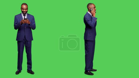 Foto de Businessman navegando por el sitio web y charlando por teléfono, utilizando el teléfono inteligente para tener una conversación remota y desplazarse a través de las redes sociales. Empleado masculino trabajando con teléfono móvil en pantalla verde. - Imagen libre de derechos