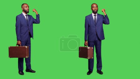 Photo for Company employee with suitcase hitchhicking on camera and doing gestures with hand over full body greenscreen. Optimistic businessman in suit waving to travel, briefcase luggage. - Royalty Free Image