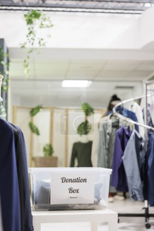 Téléchargez les photos : Vêtements d'occasion de bénévoles dans une boîte de dons dans une boutique du centre commercial. Conteneur avec vêtements usagés pour le soutien humanitaire et la réutilisation dans un magasin de mode avec personne à l'intérieur - en image libre de droit