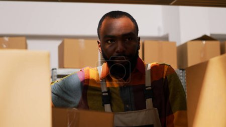 Photo for Young man organizing boxes in depot, moving cargo in cardboard packs for retail store delivery. Warehouse employee carrying packages on shelves, doing inspection. Handheld shot. Close up. - Royalty Free Image