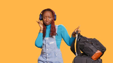 Photo for Cheerful girl dancing on mp3 music, using headset to listen to songs in studio. Young smiling person doing dance moves and having fun, listening to sounds on holiday trip. Handheld shot. - Royalty Free Image