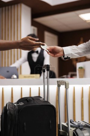 Photo for Person giving money to porter in lobby, paying cash for luxury service to carry bags and suitcases. Hotel bellboy receiving payment from guests, helping with luggage. Close up. - Royalty Free Image