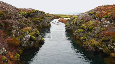 Foto de Grupo de personas de buceo de invierno en thingvellir parque cerca de reykjavik, divertirse con el deporte al aire libre en aguas frías árticas. Turistas nadando en el río helado, paisaje de hielo. Disparo de mano. - Imagen libre de derechos