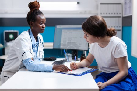 Photo for Patient signing medical application paper for emergency injury medical insurance claim after doctor check-up. Healthcare specialist aiding woman with policy medicare document - Royalty Free Image