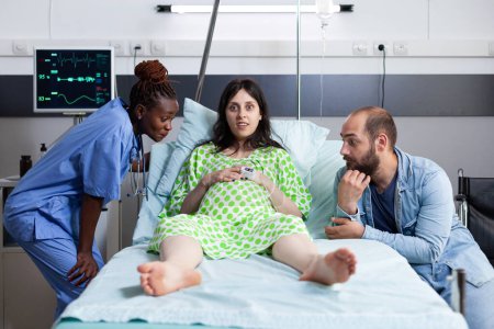 Foto de Mujer embarazada hablando con la enfermera ginecóloga durante la consulta de chequeo en la sala de hospital. Asistente de consulta de salud para paciente con embarazo embarazada. Concepto de maternidad - Imagen libre de derechos