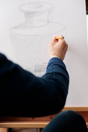 Téléchargez les photos : Gros plan du dessin à la main masculin senior avec crayon sur toile, apprendre à dessiner et dessiner, assister à un cours d'art. Artiste créant un croquis de vase tout en travaillant dans son atelier ou atelier - en image libre de droit