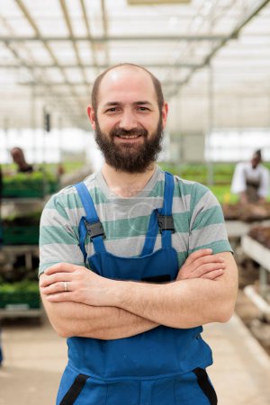 Photo for Agricultural farm worker proudly standing in front of naturally grown nutritious vegan food crops produced locally and sustainably in chemical free environmentally conscious greenhouse - Royalty Free Image