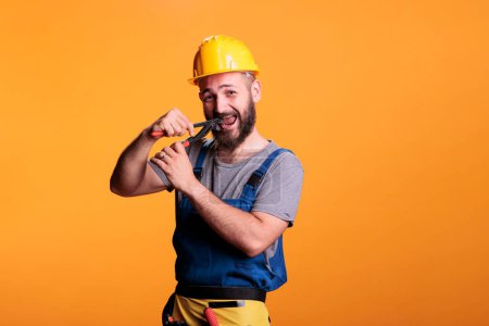 Photo for Male restore expert using pair of pliers to repair, working as carpenter or constructor in studio. Professional construction worker with hardhat holding pliers and renovating tools on background. - Royalty Free Image