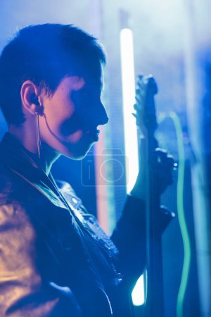 Photo for Portrait of guitarst woman playing at electricguitar adjusting sound before rock concert, composer working at heavy metal song. Superstar performer with rebel style preparing punk album in studio - Royalty Free Image