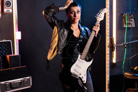 Photo for Confused rock musician having uncertain expression while standing in sound studio working at grunge album, preparing heavy metal song using electric guitar. Dont know gesture concept - Royalty Free Image
